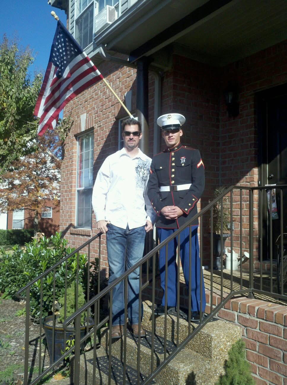 Jim Cotta standing beside his son in United States Marine Corps dress uniform beneath an American flag