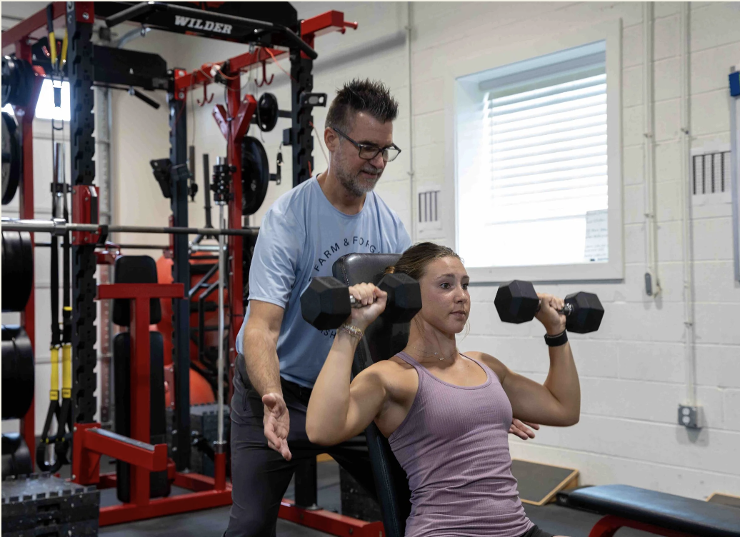 Jim Cotta spotting an athlete during an overhead press at Farm & Forge
